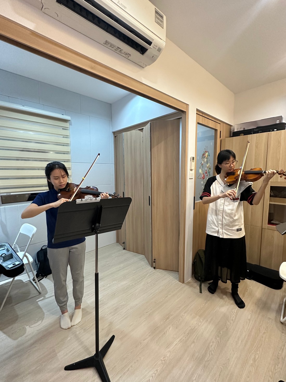 Two students playing violin together in a lesson room